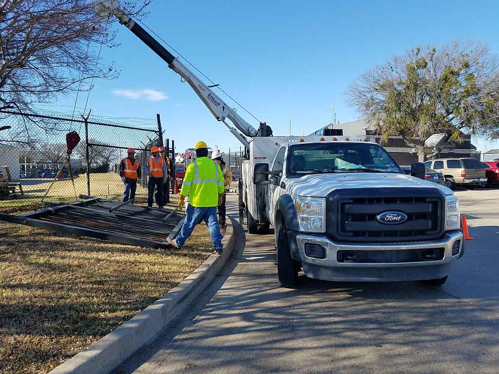 crew using a truck-mounted crane to lift a commercial security gate panel